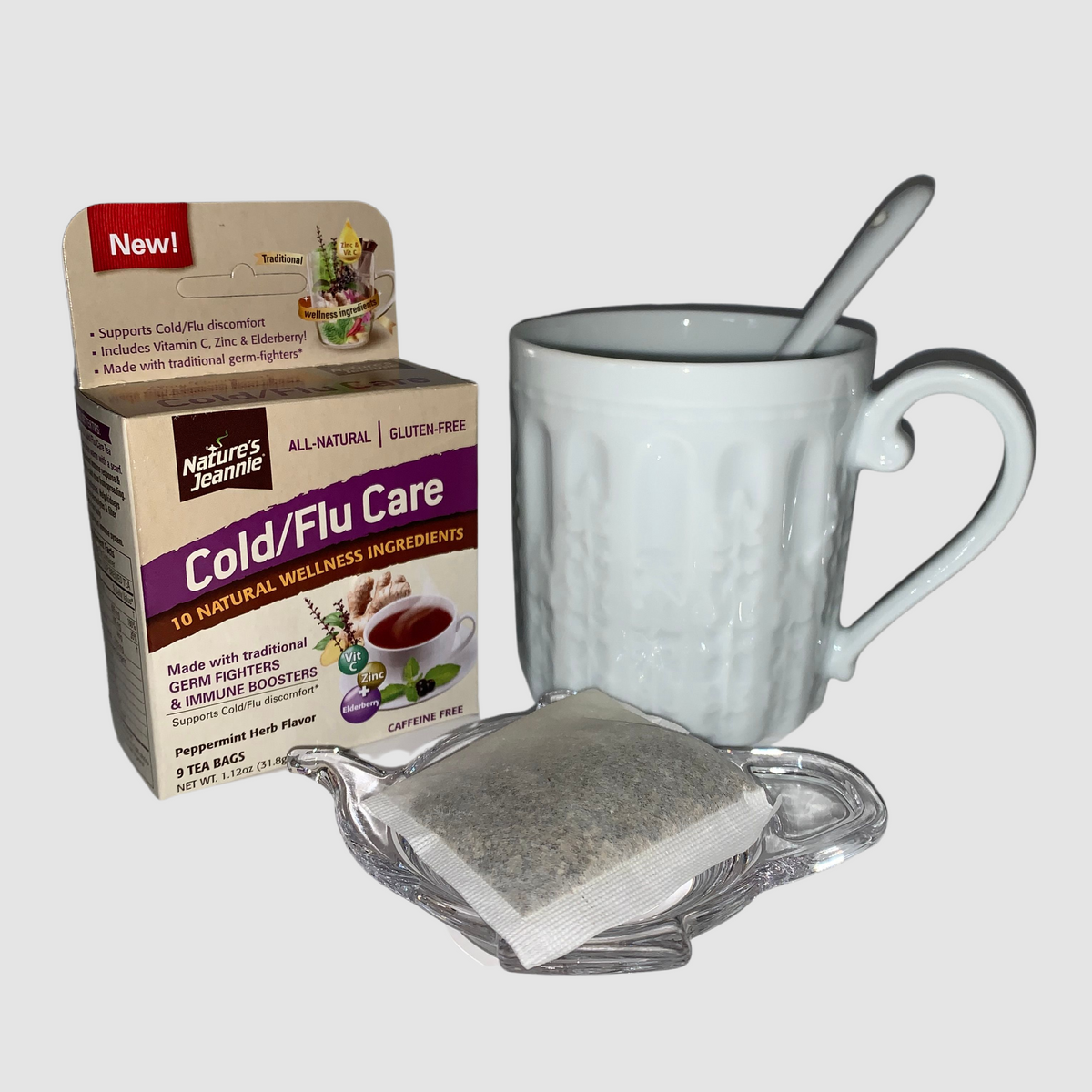 Nature&#39;s Jeannie Cold Care tea bag resting upon Nature&#39;s Jeannie tea caddy, cup and spoon.